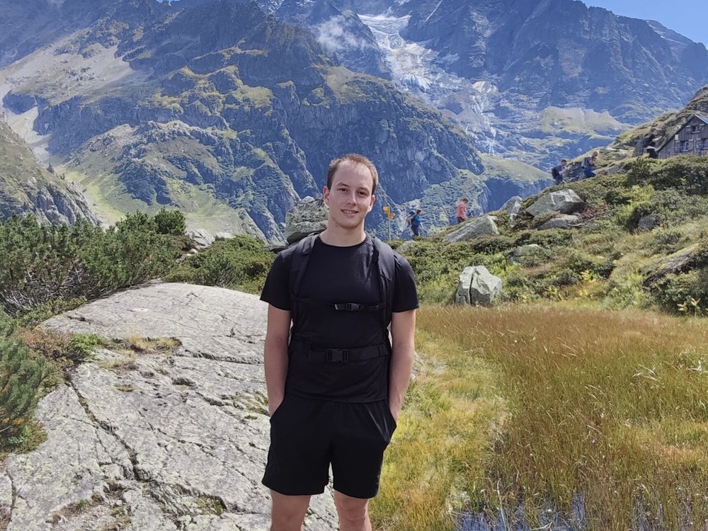 Al Depope standing on a rock slab on an alpine trail, glaciated peaks behind
