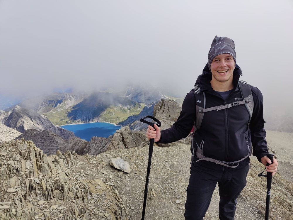 Al Depope on a misty summit with trekking poles, a turquoise reservoir far below